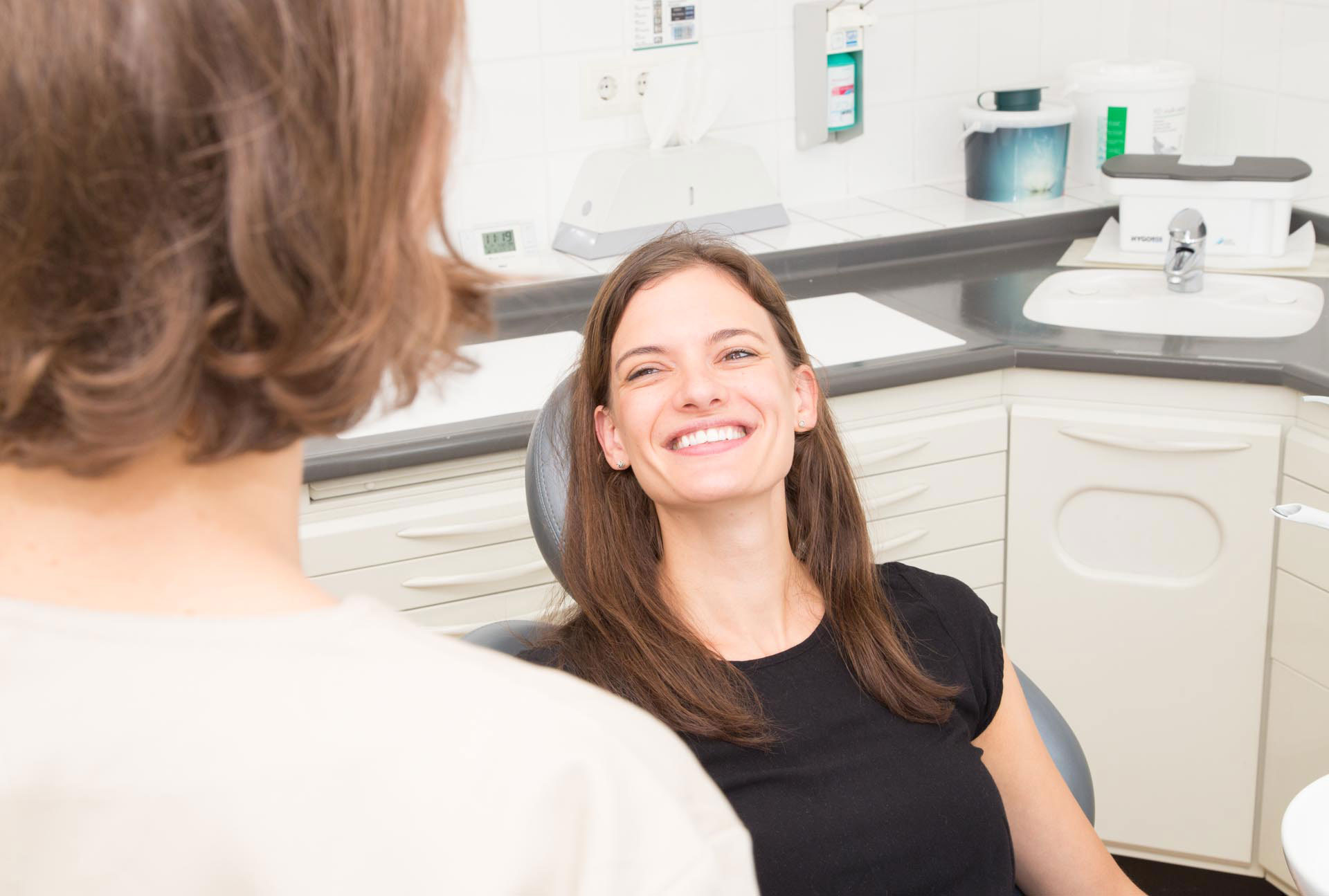 "Frau Dr. Sarah Herrmann behandelt eine lächelnde Patientin mit strahlend weißen Zähnen in einem Behandlungsraum.